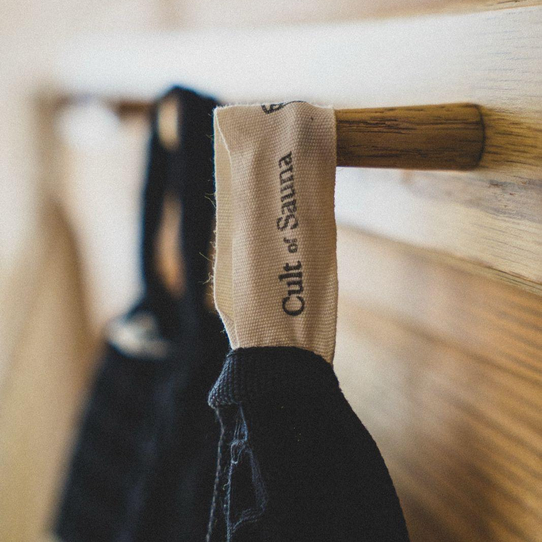 Aurora Black sauna towel hanging from its sewn-in Cult of Sauna loop on a wooden sauna peg