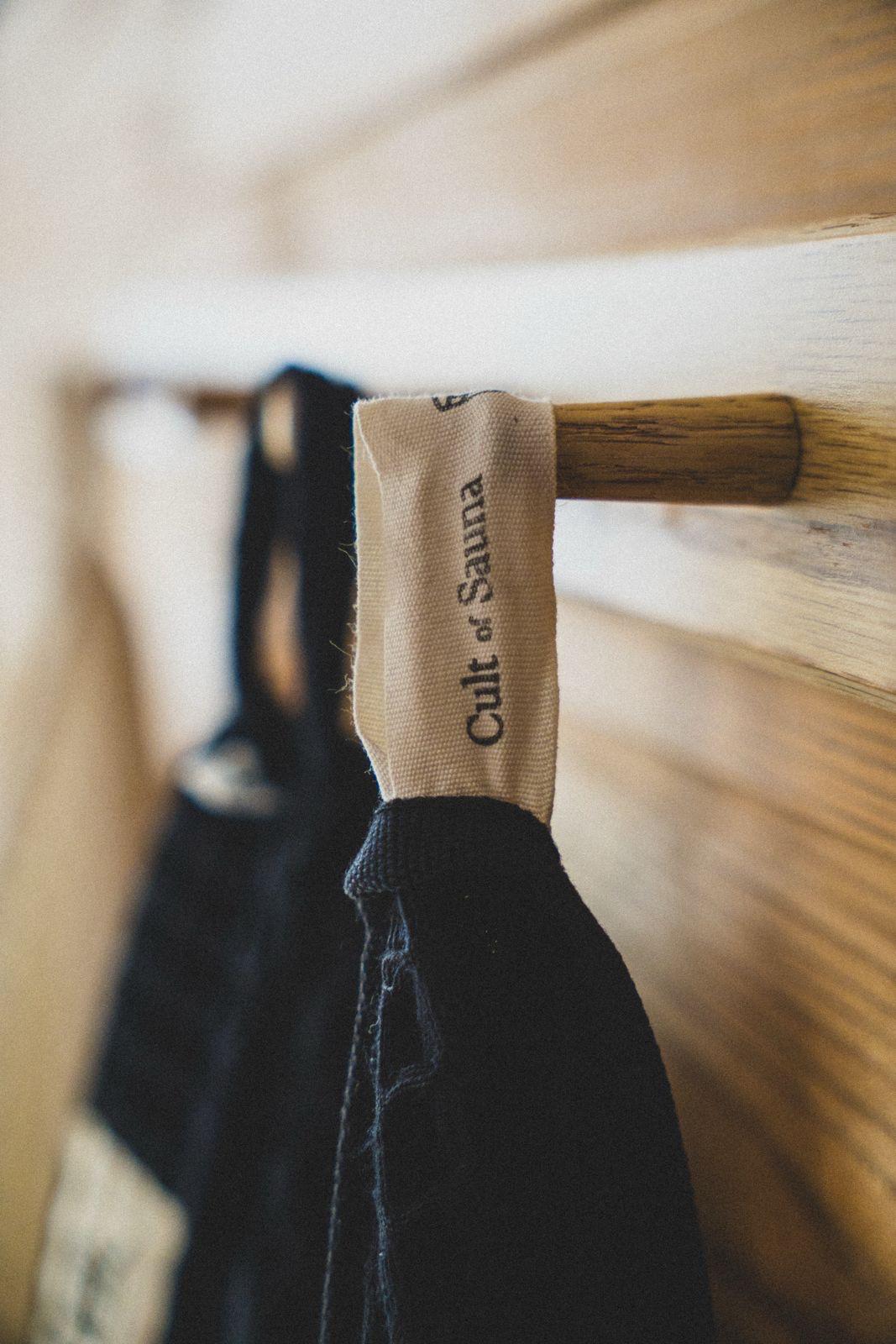 Aurora Black sauna towel hanging from its sewn-in Cult of Sauna loop on a wooden sauna peg