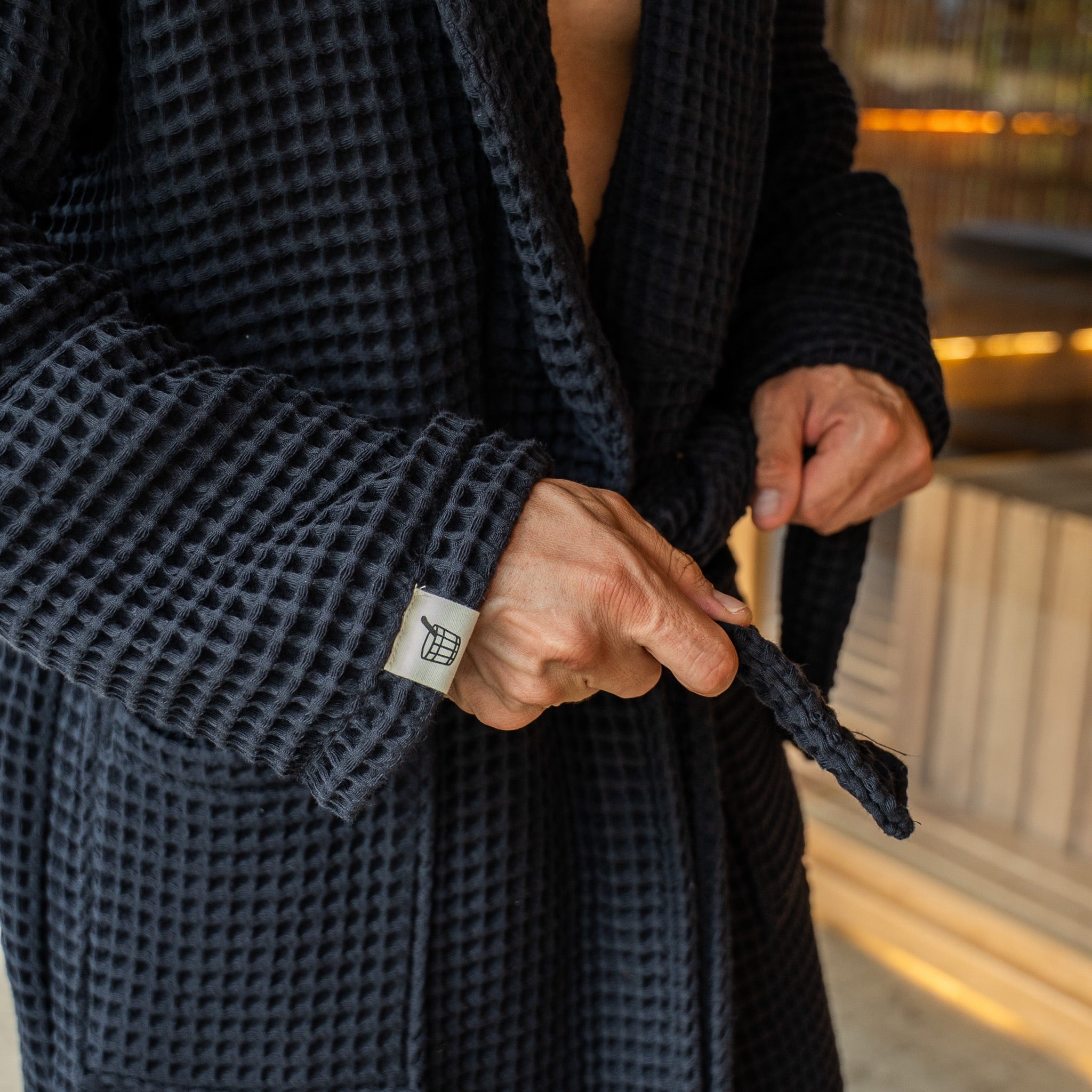 Tying the belt of The Sauna Robe in Aurora Black, waffle weave with woven Cult of Sauna cuff label