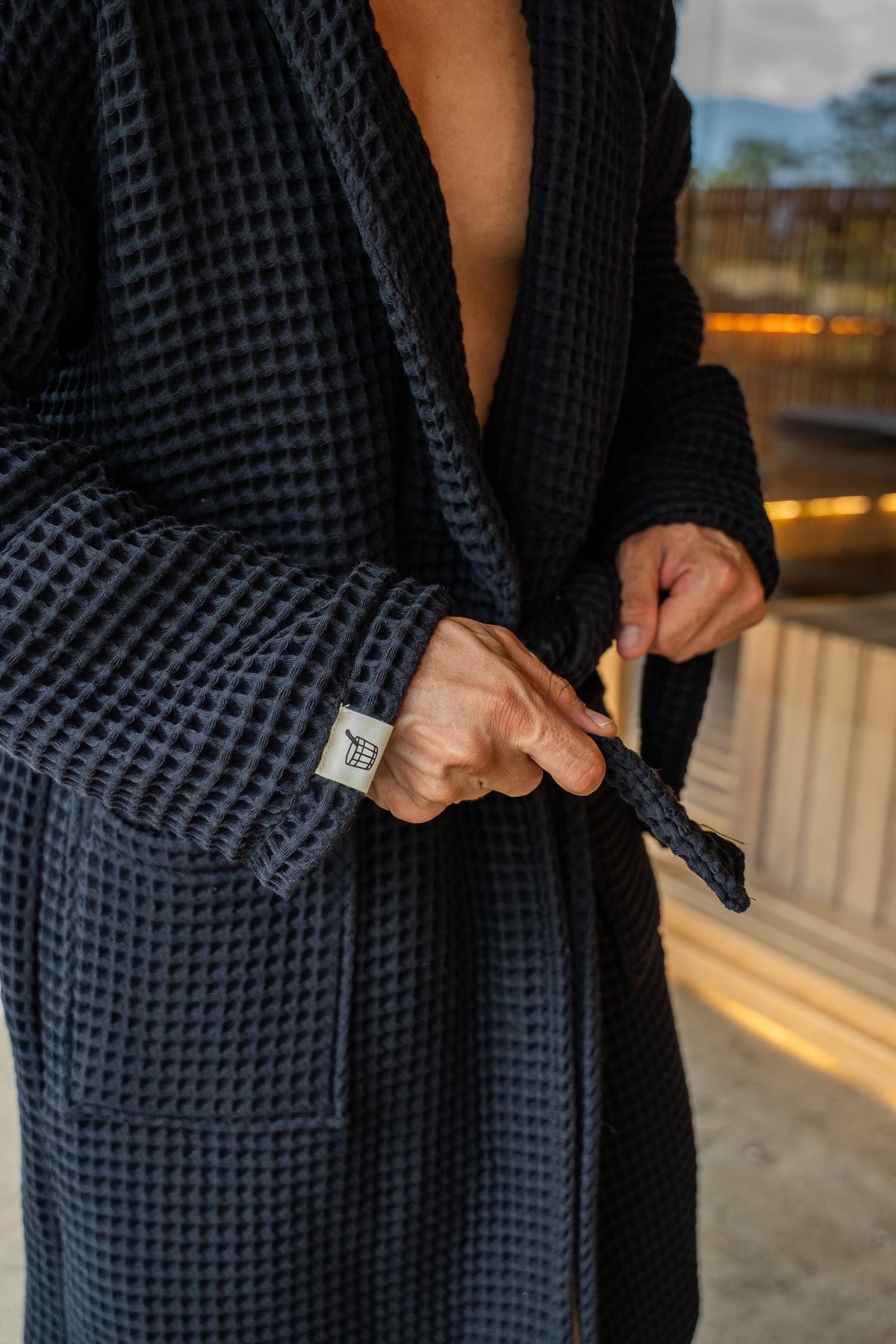 Tying the belt of The Sauna Robe in Aurora Black, waffle weave with woven Cult of Sauna cuff label